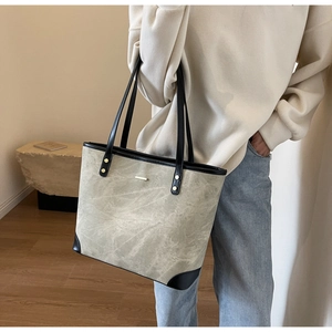 Detail of grey-green tote bag with marble texture and black leather accents on a stone