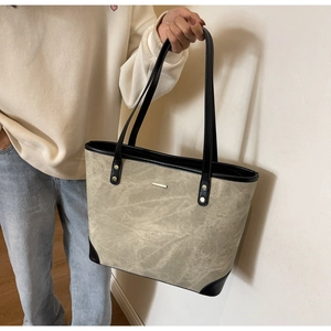 Close-up of gray tote bag featuring black leather trim and elegant gold metal bar detail