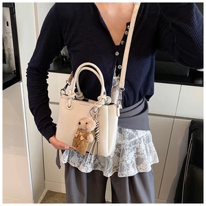 Detail of a minimalist cream bucket bag with lychee texture and cute teddy bear charm