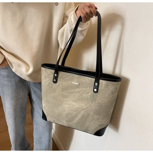 Detail of canvas tote bag with black leather trim, metal rivets and gold hardware accent