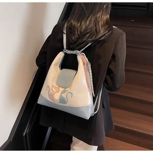 Detail of a minimalist cream and blue patchwork backpack with cat embroidery and pink tassel