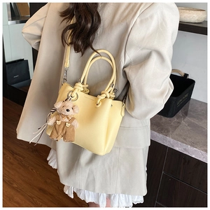 Detail of yellow lychee leather bucket bag with woven handle and plush bear charm