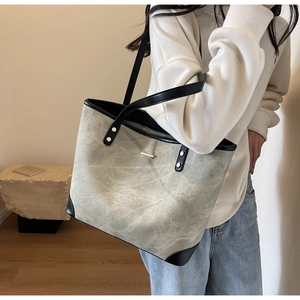 Detail of grey tote bag with black leather trim and gold hardware on female model