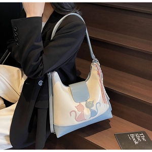 Close-up of cream and blue shoulder bag featuring cat patches and pink tassel charm