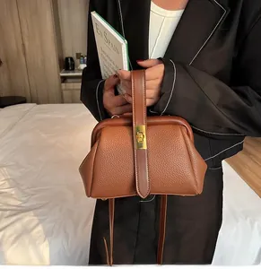 Detailed view of brown litchi grain leather handbag with gold clasp in a home setting