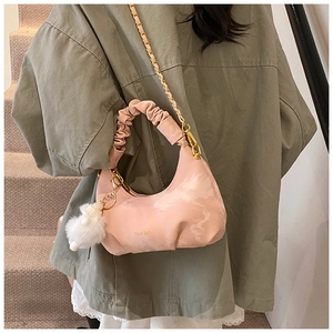 Détail du sac croissant plissé rose avec chaîne dorée et pompon blanc en scène intérieure