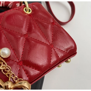 Detail of red quilted patent leather bag featuring gold hardware and pearl charm