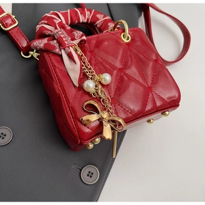 Close-up of red quilted leather bag with silk-wrapped handle and pearl bow charm