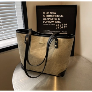 Close-up of canvas tote bag with black leather trim and gold metal logo details