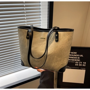 Detail of grey-green leather tote bag showing metallic accents and contrast black handles