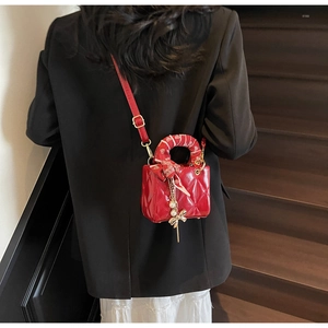 Detail of red quilted mini bag with floral scarf handle and pearl charm on a model