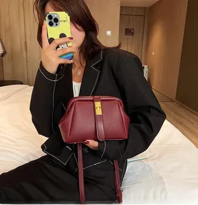 Detail of burgundy lychee grain leather crossbody bag with golden metal clasp hardware
