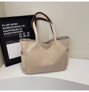 Detail of canvas tote bag showing dark brown handles and side pockets on a minimal desk