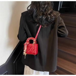 Detail of red quilted handbag with decorative silk scarf handle and pearl charm
