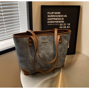 Detail of blue canvas tote bag with brown leather handles and gold metal accents