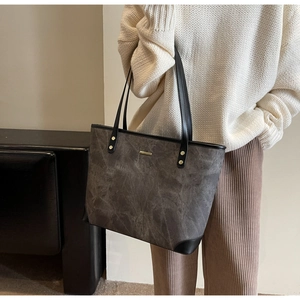 Detailed view of grey tote bag with marble texture and black straps worn by model