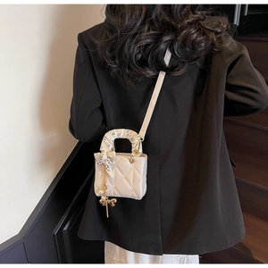 Close-up of cream quilted handbag with silk scarf handle and golden pearl pendant