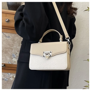Detail view of contrast leather handbag with silver metallic buckle on light wood background