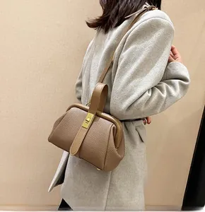 Close-up of brown litchi pattern leather handbag with gold metal buckle and gray coat