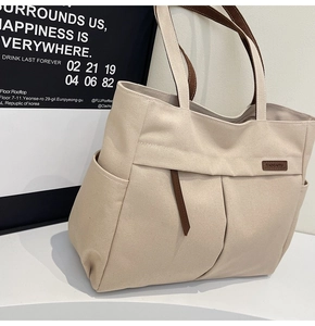 Detailed close-up of canvas tote bag with brown leather straps and side utility pocket
