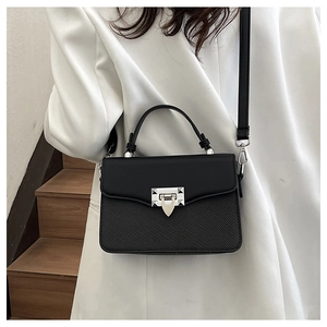 Detail of minimalist black crossbody bag with silver V-buckle on white coat