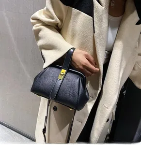 Detail of black lychee grain leather handbag with gold clasp on a cream coat