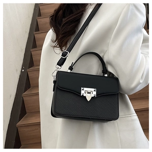 Detail of black crossbody bag with silver buckle worn by model against stairs