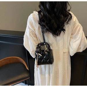 Close-up of black quilted leather handbag featuring a silk scarf handle and gold hardware