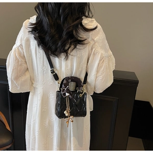 Detail of black quilted shoulder bag with patterned silk scarf and pearl butterfly charm
