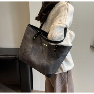 Detail of large brown suede tote bag with gold metal trim and black leather handles