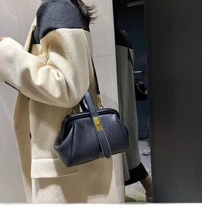 Detail of black lychee grain leather handbag with gold metal clasp on a beige coat