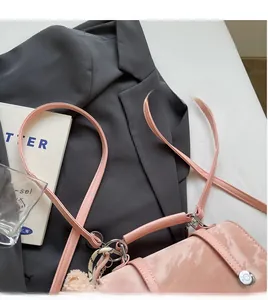 Detailed view of pink glossy handbag with long shoulder strap and fluffy ball charm