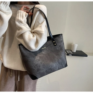 Detail of grey tote bag with black leather straps and gold metal trim in a lifestyle setting