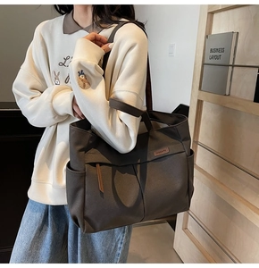 Detail view of large brown canvas tote bag with side pocket and premium leather label