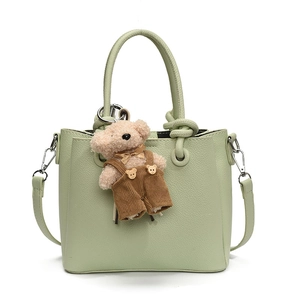 Chic light green bucket handbag with textured leather finish and cute teddy bear charm