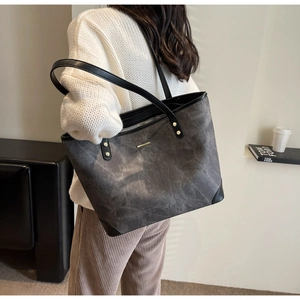 Detailed side view of grey textured tote bag with gold metal trim and black straps