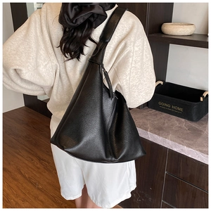 Detail of black litchi grain leather tote bag showing wide shoulder strap on a model