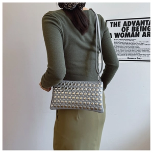 Detail of grey leather shoulder bag with silver rivet studs on a model in olive green