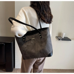 Detail of dark grey washed tote bag with black leather straps and gold rivets on a model