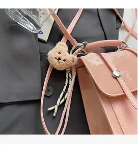 Pink patent leather crossbody bag with a plush bear charm and woven rope detail