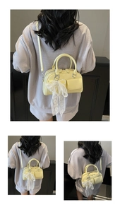 Detail of pale yellow Boston bag featuring a white lace bow and adjustable shoulder strap