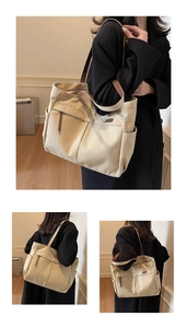 Detail view of large canvas tote bag with brown leather straps and exterior pockets