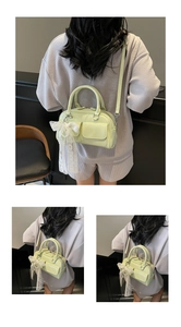Detail view of mint green patent leather Boston bag with a white lace bow and pearl charm