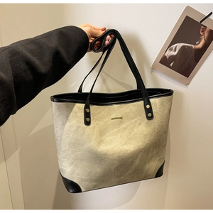 Detail of canvas tote bag with black leather trim and subtle gold metal logo accent