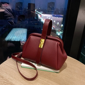 Deep red lychee textured leather handbag with gold twist lock and top handle in city light