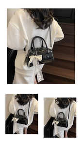 Detail of a black leather Boston bag with a decorative lace bow and pearl charm