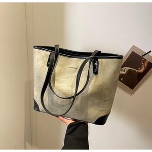 Detail of grey-brown canvas tote bag with black leather trim and gold metal accent