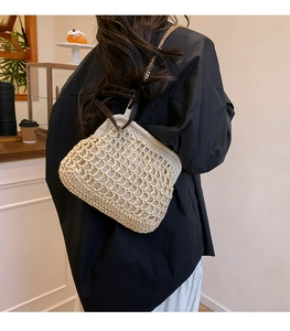 Beige woven straw shoulder bag with gold chain strap in a cozy cafe setting