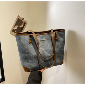 Detail of dark grey denim tote bag with brown leather handles and metal brand plate