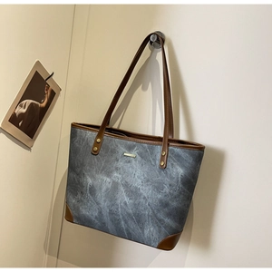 Detail of grey washed canvas tote bag with brown leather handles and metal bar accents